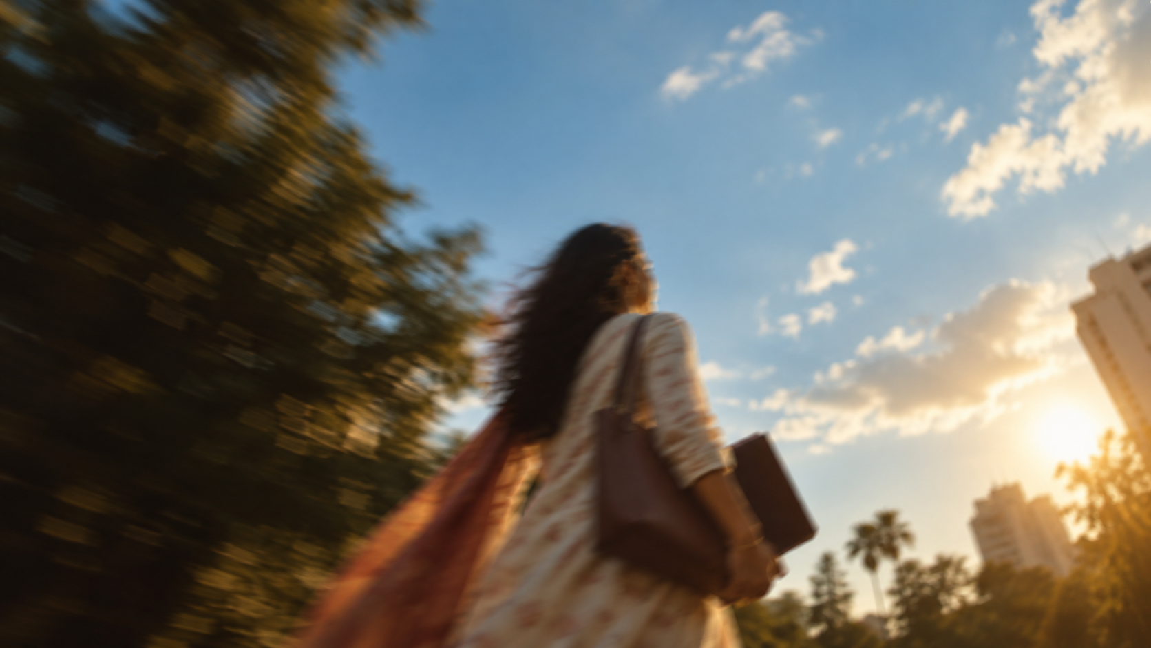 A woman walking into late sun, a diary under her arm